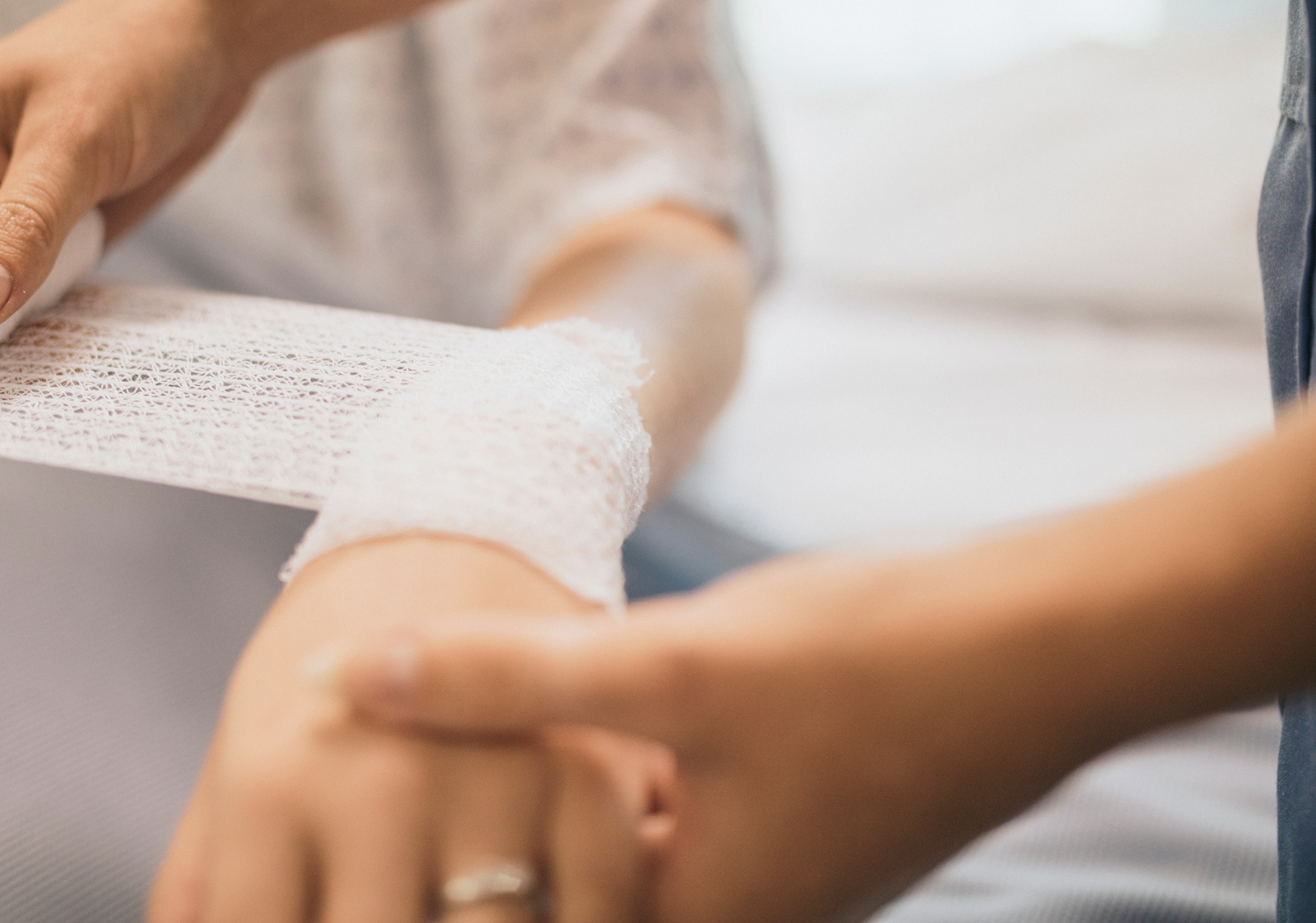 Eine Pflegefachkraft versorgt eine Wunde an der Hand eines Patienten. Symbolisiert professionelles Wundmanagement und Verbandwechsel in der häuslichen Pflege.